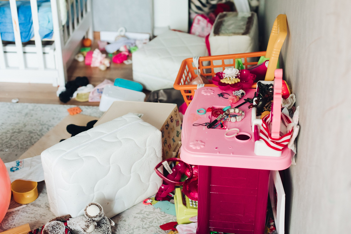 Unordentliches Kinderzimmer mit Spielzeug und Matratzen auf dem Boden.
