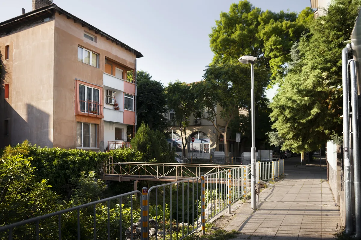 Bürgersteig mit Metallzaun neben mehrstöckigem Wohngebäude.